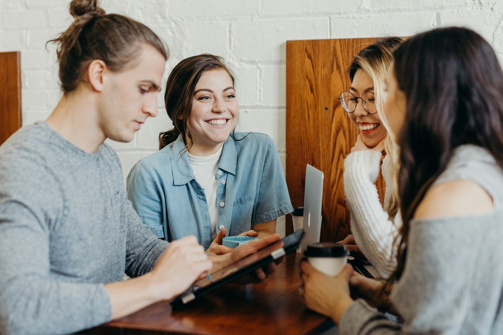Four friends laughing together around a table with a laptop and phone